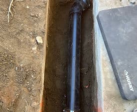 Black drainage pipe installed in a trench, showing surrounding dirt and construction materials.