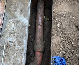 Exposed underground pipe during plumbing repair, surrounded by dirt and tools.