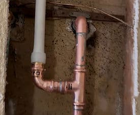 Copper plumbing installation with a light fixture in a wall cavity.