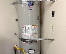 Gray water heater installed in a small utility area with safety labels and connections visible.