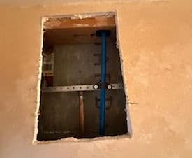 Visible plumbing access point in a wall with copper and blue pipes.
