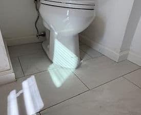 White toilet in a bathroom with tiled floor and sunlight casting a shadow.