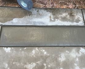 Freshly poured concrete slab with a textured finish and a wheelbarrow in the background.
