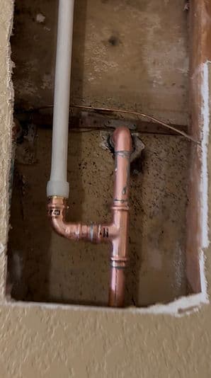 Copper plumbing pipes in a wall cavity, with visible mold and damage around the opening.