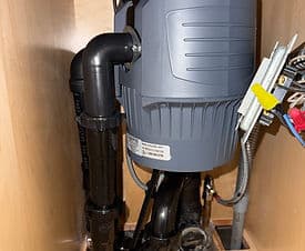 Under-sink garbage disposal unit with plumbing connections and electrical components visible.