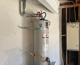 New water heater installation in an unfinished basement with exposed plumbing.