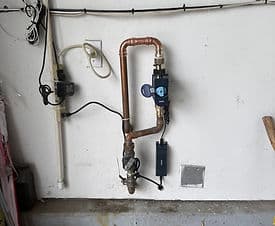 Copper plumbing with water meter and sensor mounted on a garage wall.